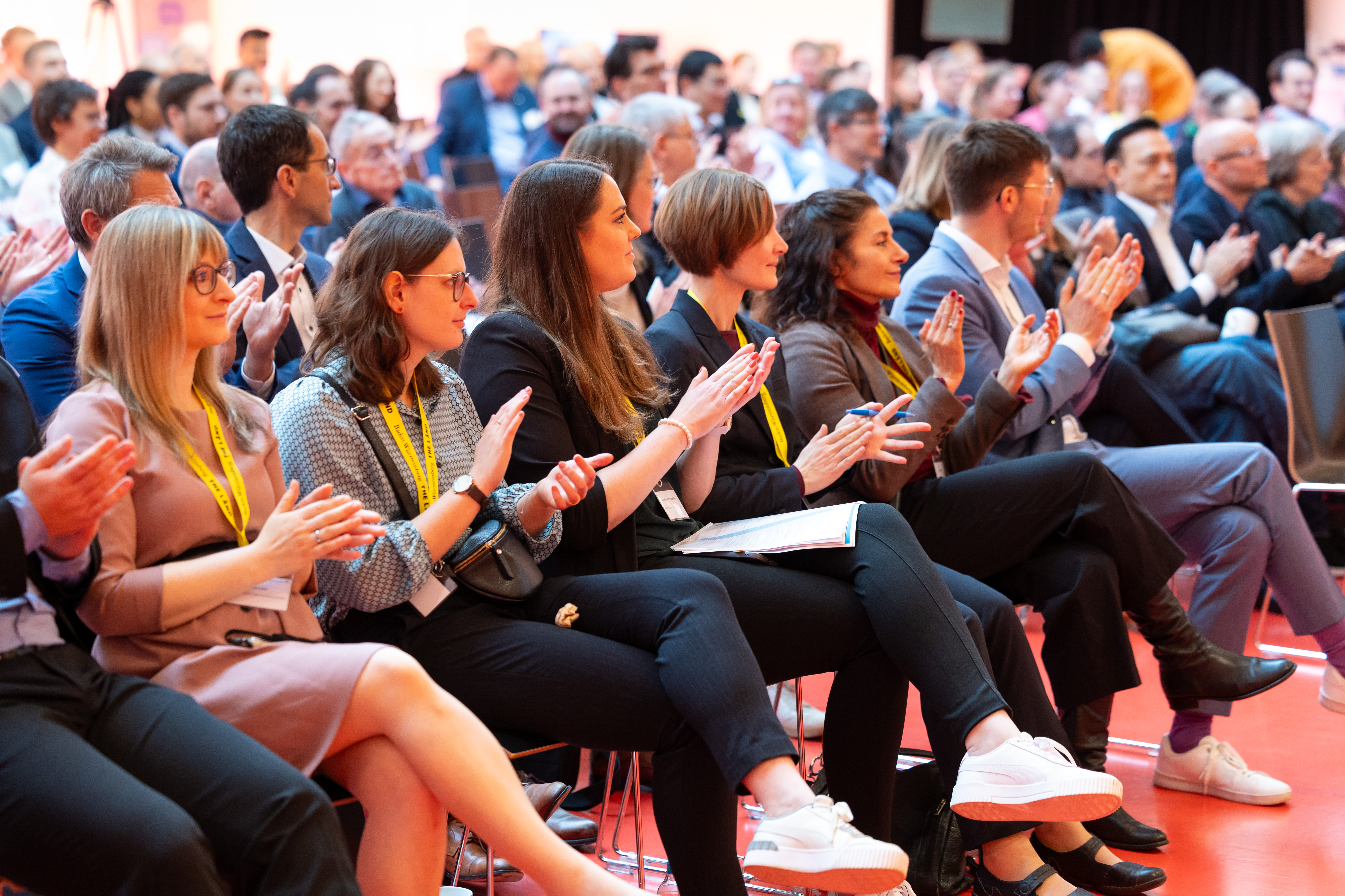 Personen in formeller Kleidung applaudieren im Sitzen.