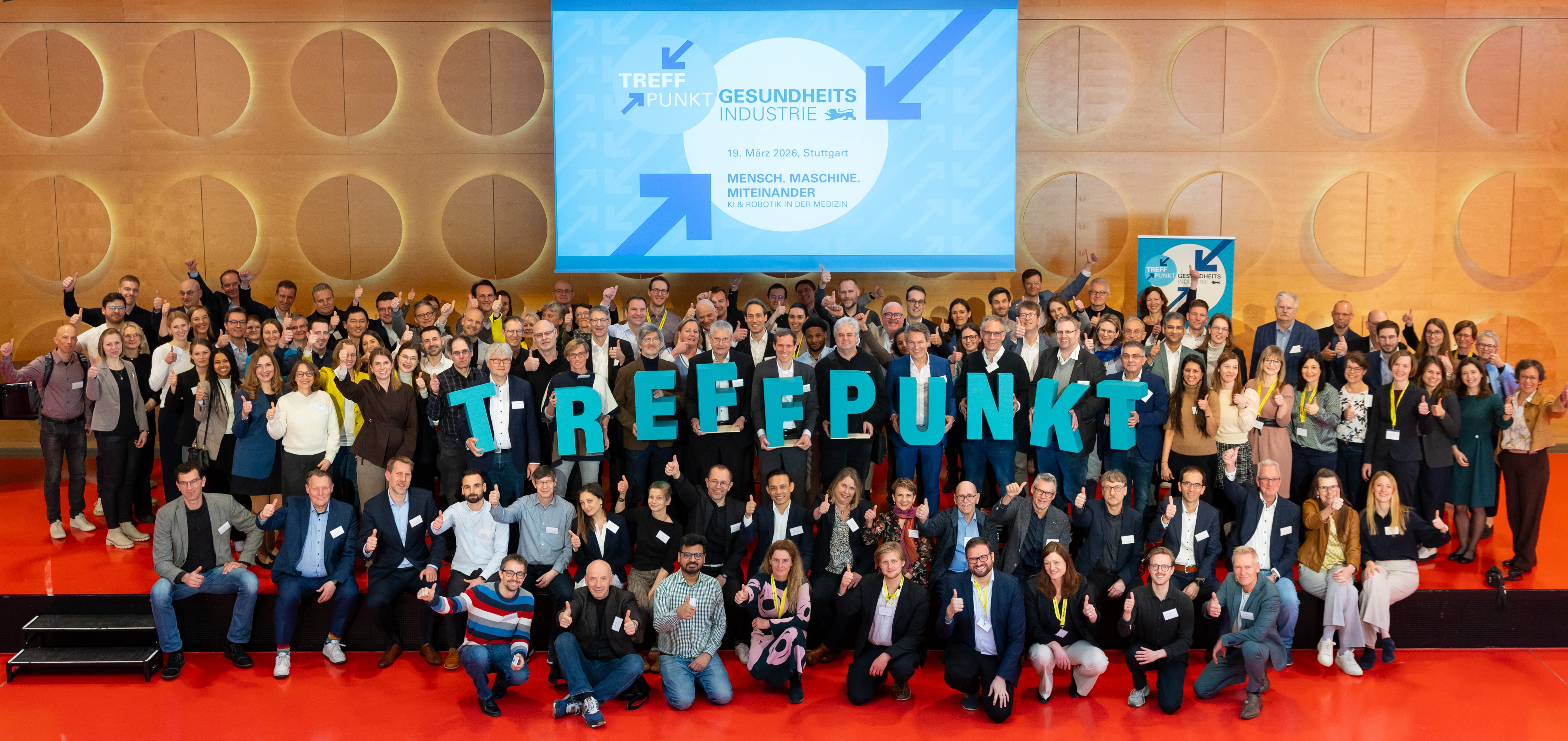 Eine große Personengruppe auf der Bühne für ein Gruppenbild. Sie halten die Buchstaben T-R-E-F-F-P-U-N-K-T nach oben.