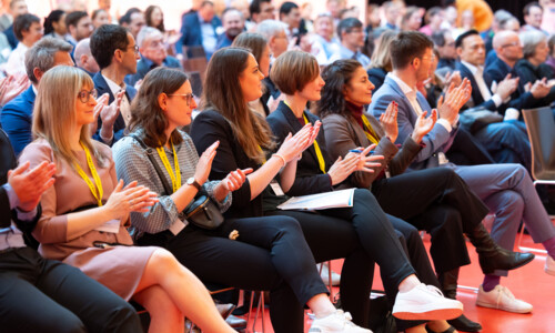  Personen in formeller Kleidung applaudieren im Sitzen.