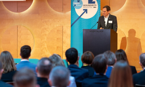 Zwei Männer sitzen auf der Bühne in Sesseln, einer spricht mit einem Mikrofon, der andere hört zu. Im Vordergrund sind große Buchstaben mit dem Wort „TREFFPUNKT“ zu sehen.