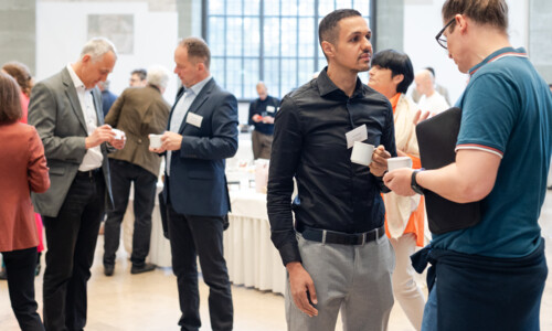 Networking und Kaffeepause beim Treffpunkt Gesundheitsindustrie 2025 Mehrere Personen unterhalten sich in einem Veranstaltungsraum bei einer Kaffeepause und halten Tassen in der Hand. Im Hintergrund stehen weitere Teilnehmende an Stehtischen.