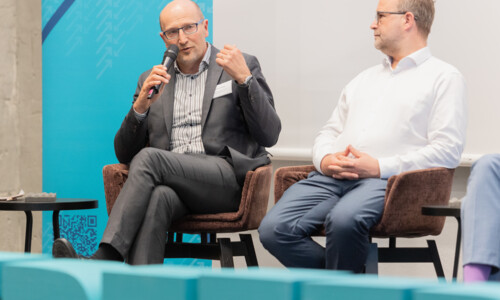 Podiumsgespräch auf dem Treffpunkt Gesundheitsindustrie 2025 Zwei Männer sitzen auf der Bühne in Sesseln, einer spricht mit einem Mikrofon, der andere hört zu. Im Vordergrund sind große Buchstaben mit dem Wort „TREFFPUNKT“ zu sehen.