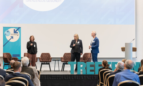 Abschlussdiskussion beim Treffpunkt Gesundheitsindustrie 2025 Drei Personen stehen auf einer Bühne vor einem Publikum und sprechen mit Mikrofonen, im Hintergrund Banner und große Buchstaben mit dem Wort „TREFFPUNKT“.