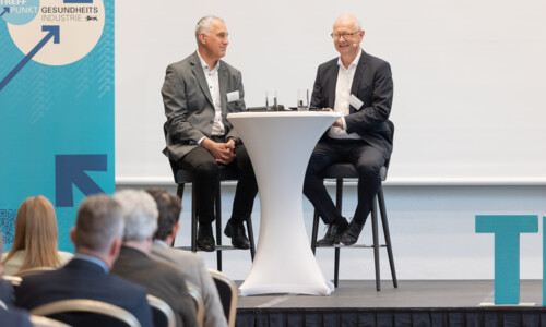 Interview beim Treffpunkt Gesundheitsindustrie 2025 Zwei Männer sitzen auf einer Bühne an einem Stehtisch und sprechen vor Publikum, daneben ein Banner mit der Aufschrift „Treffpunkt Gesundheitsindustrie“.
